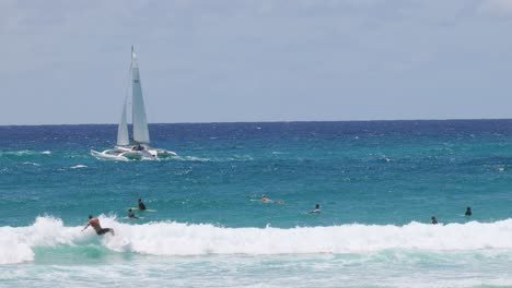 sailboat cruising past surfers on vibrant ocean waves