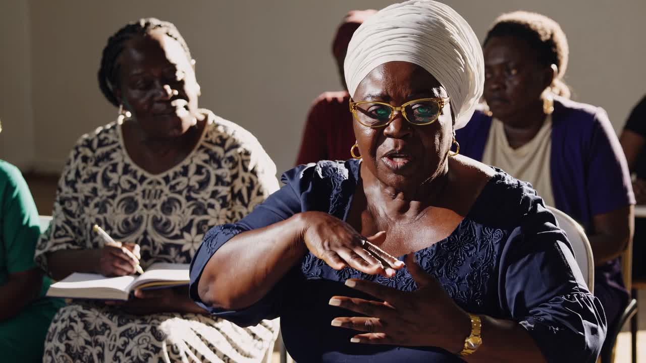 Un video en plano medio captura a un grupo de mujeres escuchando atentamente en una habitación iluminada por el sol.