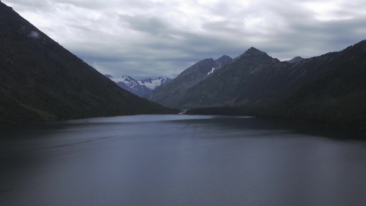 Tranquille riprese aeree sulla superficie scura dell'acqua dei Laghi Multinskie, Repubblica dell'Altai, Russia, circondati da pendii montani boscosi in una giornata nuvolosa