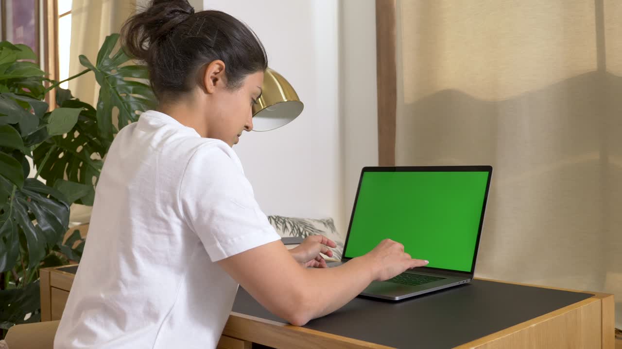 una joven india usa una computadora con una pantalla verde chromakey. habitación brillante y acogedora en el hogar. educación en el hogar aprender a conocer y financiar