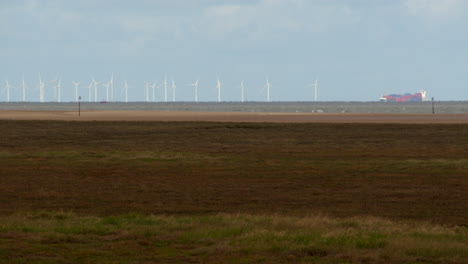 Wide-shot-of-tidal-mud-flats-with-wind-turbines-and-cargo-ship-in-background-at-Saltfleet,-Louth,-Lincolnshire