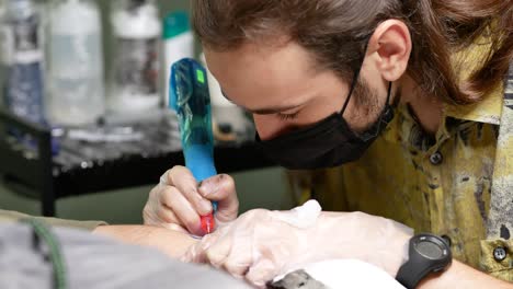 Male-tattooist-making-tattoo-on-hand-of-client