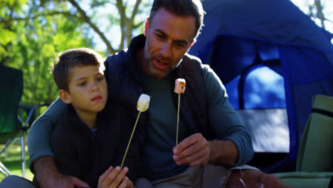 father and son roasting marshmallows outside the tent