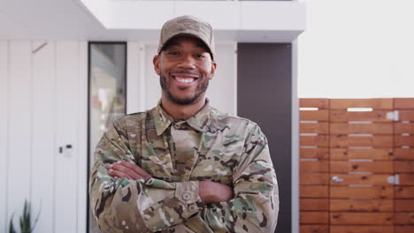 Millennial-black-male-soldier-steps-towards-camera,-crosses-arms-and-smiles-to-camera,-close-up