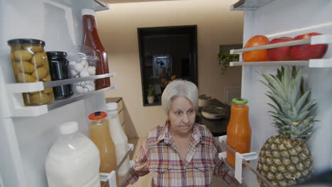 an elderly woman looks into the refrigerator, inside view