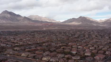 Toma-Aérea-De-Primer-Plano-Del-Cañón-De-Roca-Roja-Detrás-De-Los-Suburbios-Del-Desierto-En-Las-Vegas,-Nevada