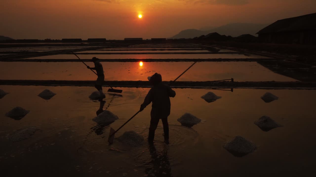 오후 늦게 부드러운 석양 태양 에 소금 을 수확 하기 위해 소금 을 준비 하는 두 명 의 노동자 의 실루 ⁇