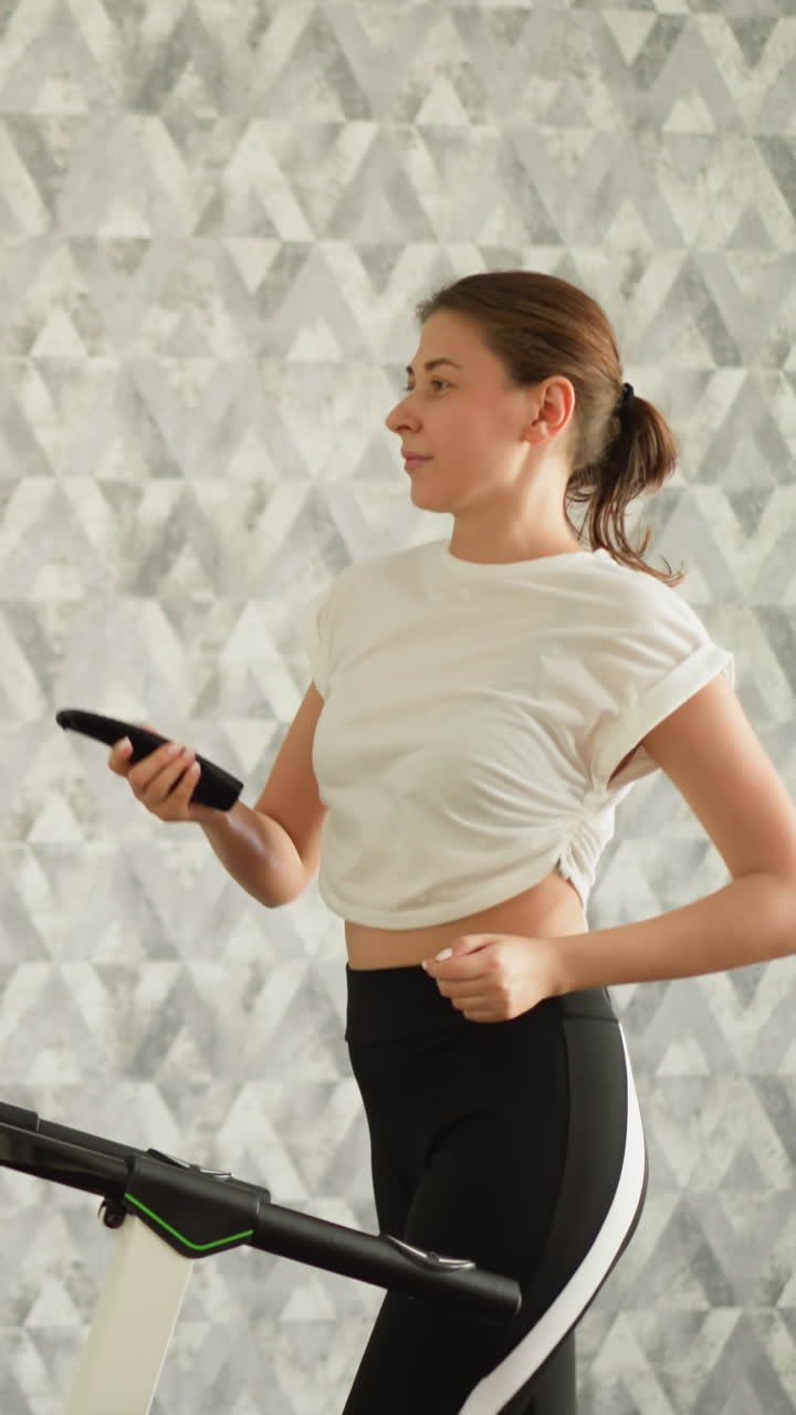 mujer con control remoto en la cinta de correr en casa. deportiva enciende la televisión durante el entrenamiento de cardio en la máquina en la casa. deportista agrega diversión al entrenamiento