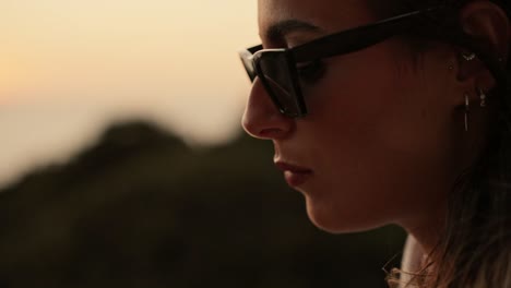 primer plano de la cara de una mujer joven con gafas de sol comiendo un dulce al atardecer