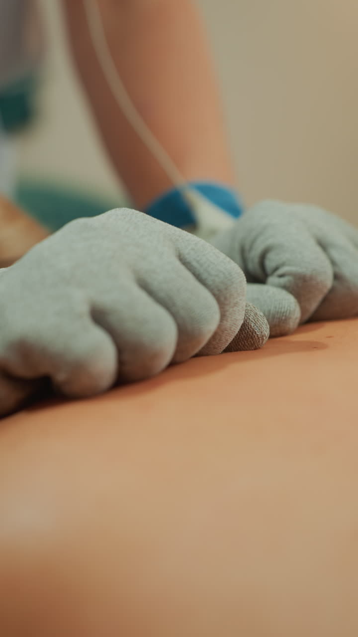 Mikrostrømshandske-massage på bar ryg, kosmetolog påfører pulserende elektroder med handskeklædte hænder, varm klinikbelysning, nærbillede af rygsøjleområdet, blidt tryk og glid, muskelafslapning, hud.
