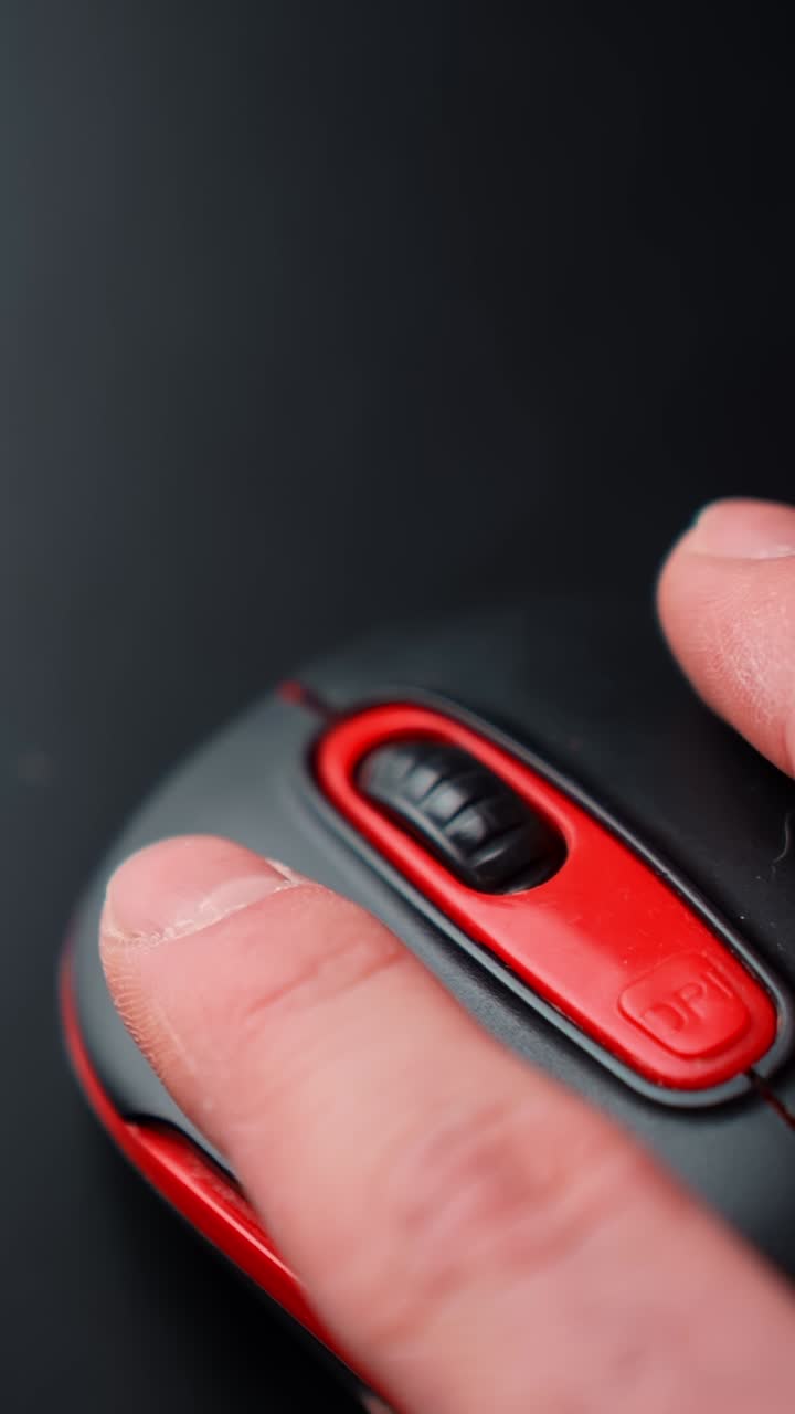 Vertical macro of a finger pressing the DPI button on a red and black computer mouse on a dark desk, soft studio lighting, minimal tech vibe with copy space