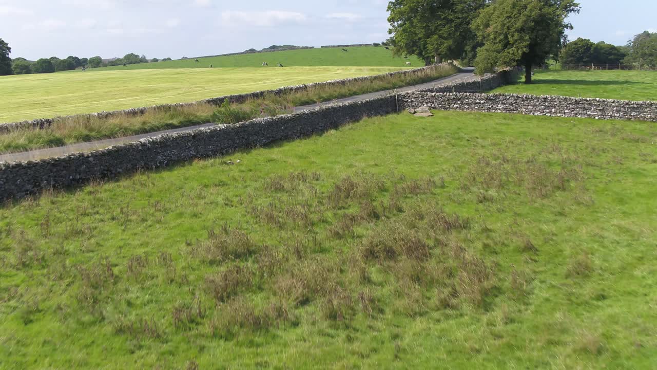 imágenes de drones sobre un campo de una granja en el campo del norte de yorkshire acercándose y volando sobre una ondulada carretera de campo, ascendiendo y panoramizando para revelar más de la carretera y las colinas en la distancia