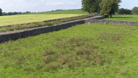 Drohnenaufnahmen-über-Einem-Landwirtschaftlichen-Feld-In-Der-Landschaft-Im-Norden-Von-Yorkshire,-Die-Sich-Einer-Hügeligen-Landstraße-Nähern-Und-Darüber-Fliegen,-Aufsteigen-Und-Schwenken,-Um-Mehr-Von-Der-Straße-Und-Den-Hügeln-In-Der-Ferne-Sichtbar-Zu-Machen