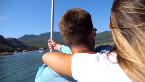 rear back view of young unrecognizable couple spending time together on deck of sailboat at sunny day. beautiful girl hugging her boyfriend from behind on boat during trip. vacation or holiday concept. close up