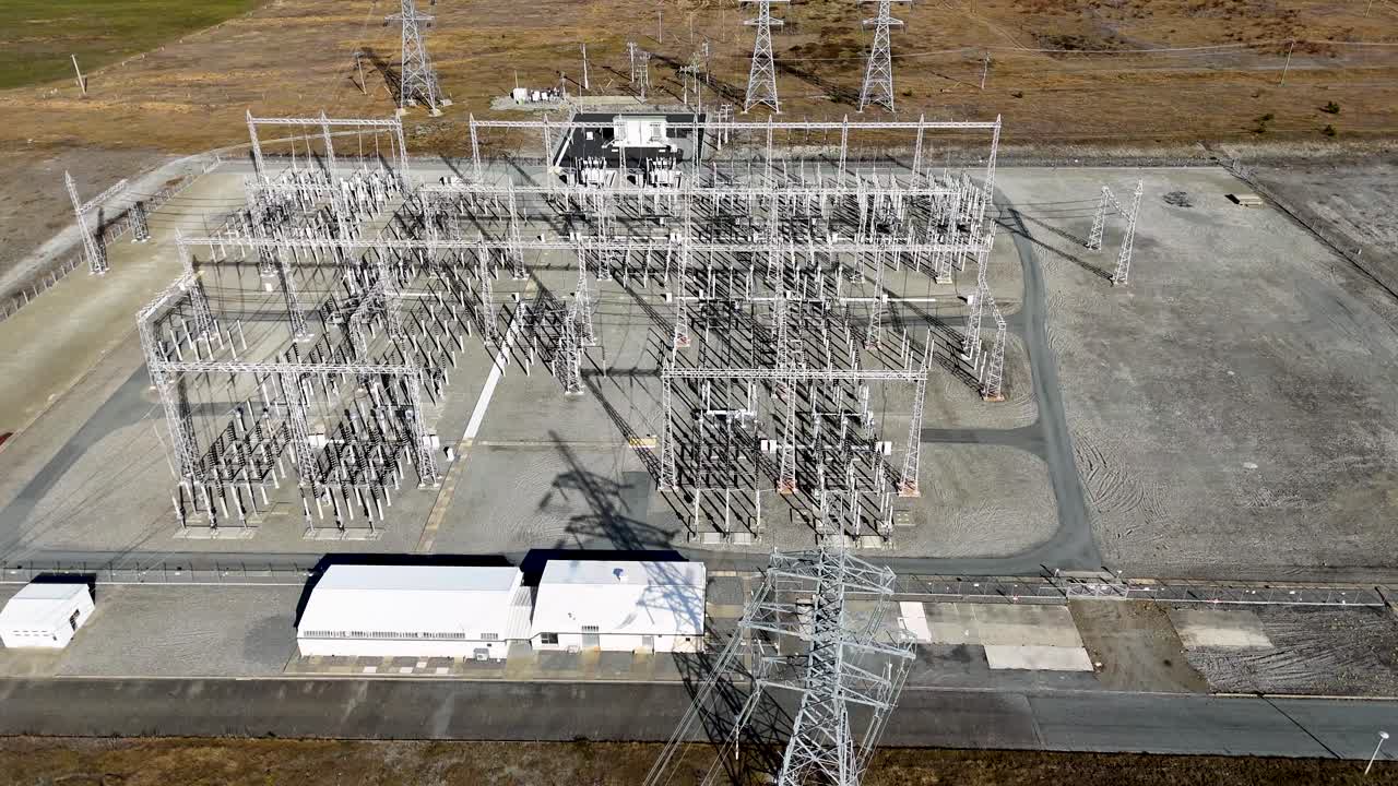 Drone footage captures a vast electrical substation at Lake Tekapo, showcasing intricate power lines and transformers under clear skies