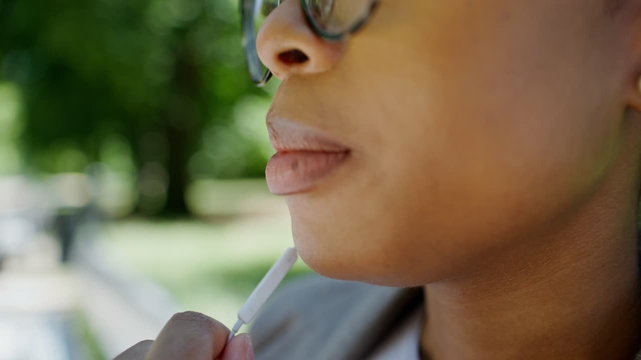 mujer aplicando lápiz labial o usando auriculares al aire libre