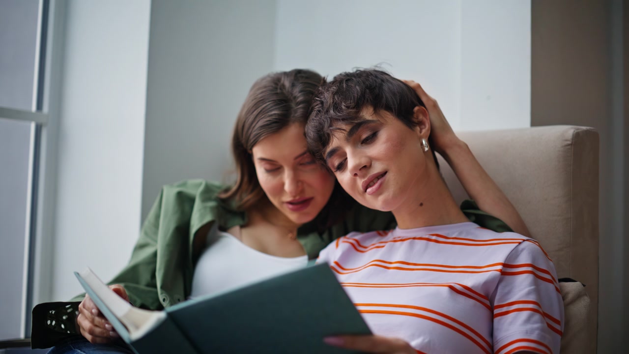 Dos mujeres viendo fotos sentadas en casa en primer plano. Pareja lesbiana hojeando un álbum.