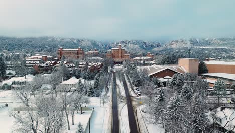 drone reverse dolly along straight snow covered road away from hotel passing neighborhood in colorado