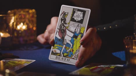 primer plano de una mujer dando una lectura de cartas del tarot en una mesa a la luz de las velas sosteniendo la carta de la muerte 5