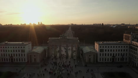 Antena:-Puerta-De-Brandenburgo-En-Berlín-Con-Multitud-De-Personas,-Turistas-En-El-Suelo-En-La-Hermosa-Luz-Del-Atardecer