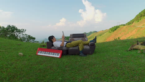 young musician laid on couch sofa outdoor in nature while writing a song