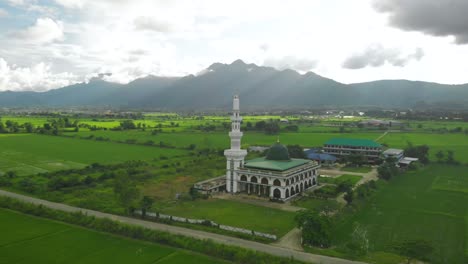 muslim mosque on the grass land, green grass, mountain background thailand, aerial drone shot orbiting right, day light cloudy day