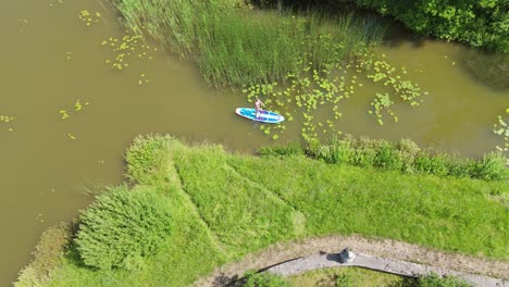 flying above young woman stand up paddling on sup board on pond in summer