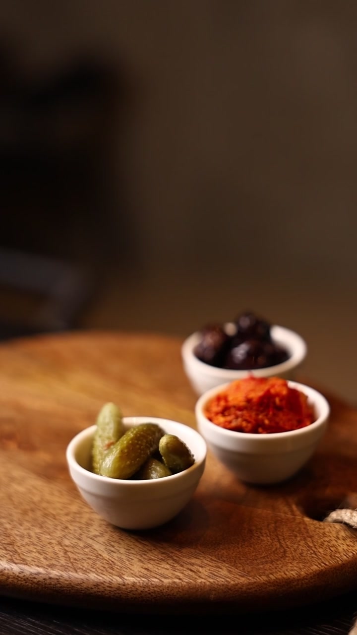 Small Bowls of Pickles, Olives, and Spiced Paste on a Wooden Board