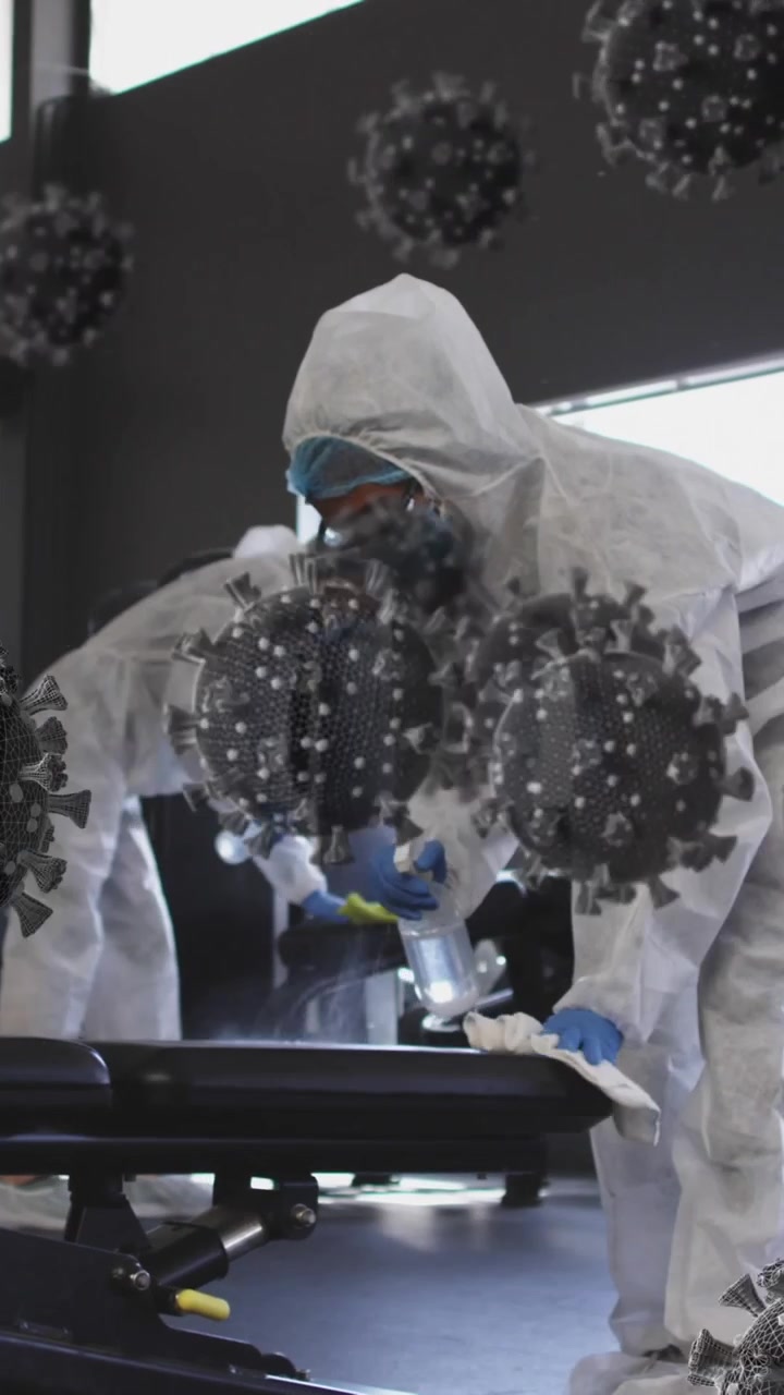 Molteplici cellule COVID-19 che fluttuano sopra un gruppo di operatori sanitari che puliscono la palestra usando disinfettante.