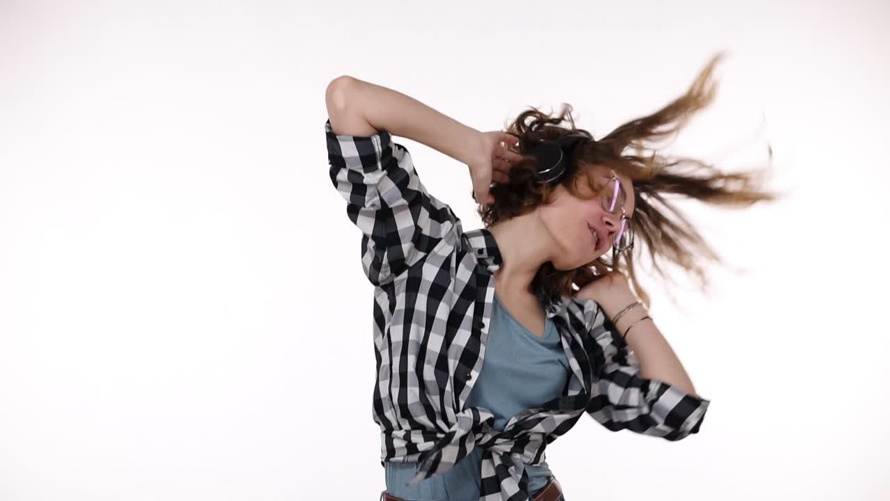 Relaxed, cheerful woman listening her favourite song on smartphone dancing with closed eyes while enjoying music with headphones over white background. Concept of emotions
