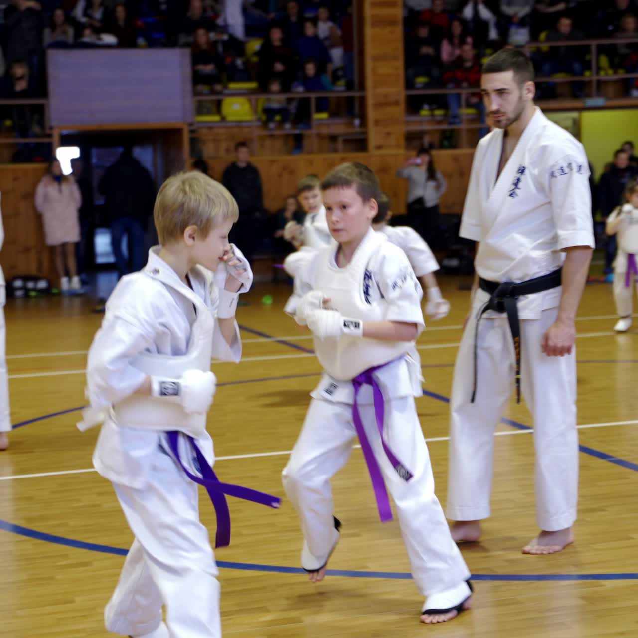 Young athletes sparring supervised by adult trainers. Boys divided into pairs to practice karate moves