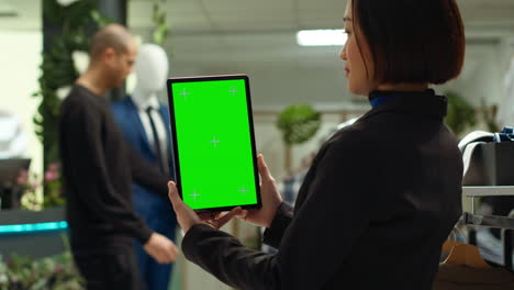 mujer de negocios sosteniendo una tableta de pantalla verde en una tienda de moda