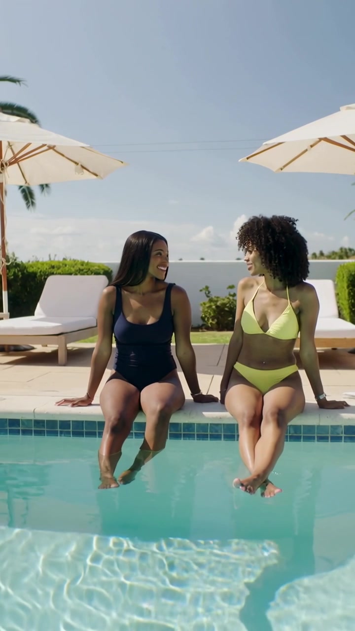 Vertical video: Turning, two women chatting to catch up at pool edge, wearing swimsuits