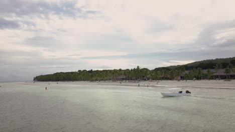 Panoramic-View-Of-Tropical-Beach-With-Tourist-Boat-Near-The-Shore-On-A-Cloudy-Day---aerial-drone-shot