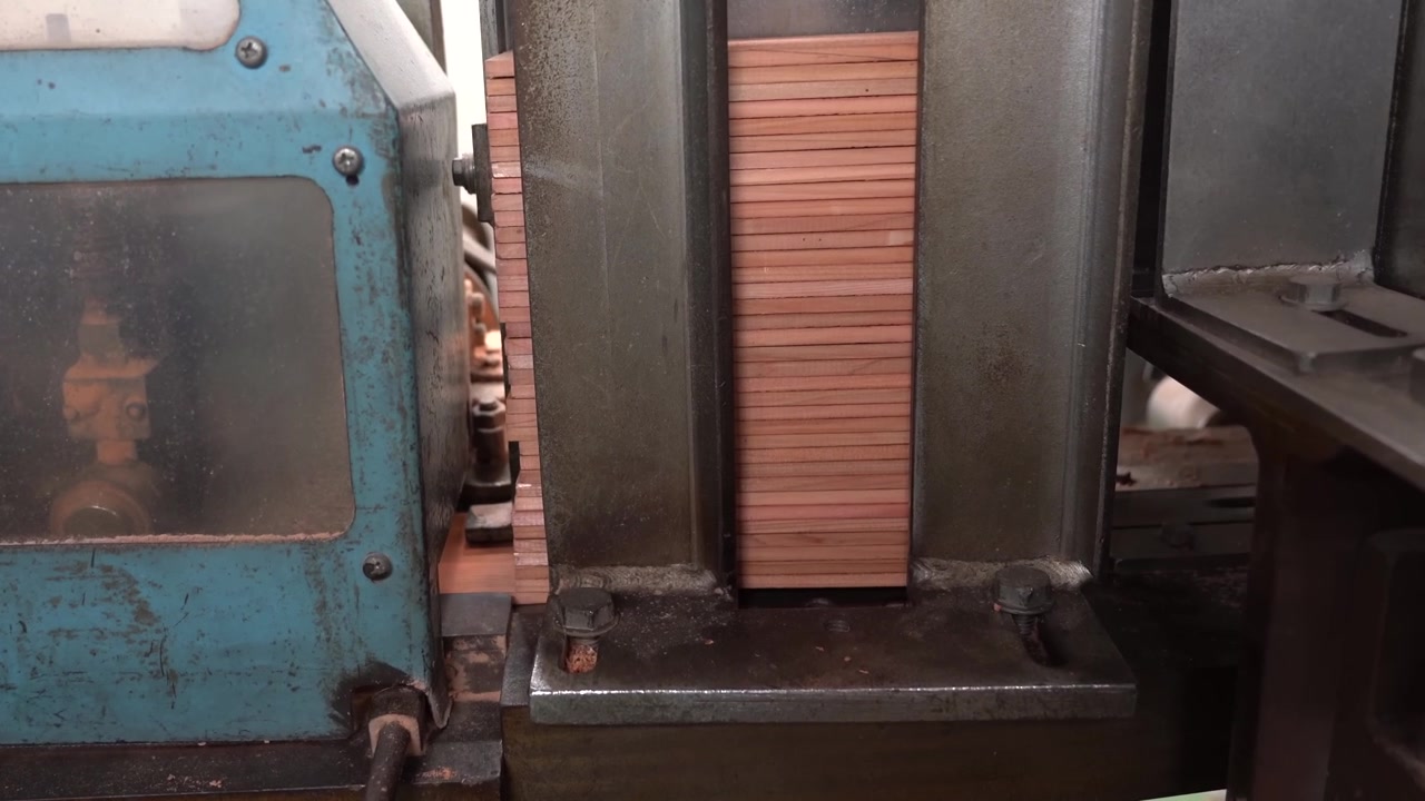 Macchina che pressa listelli di legno impilati per matite tra morsetti metallici all'interno di una fabbrica