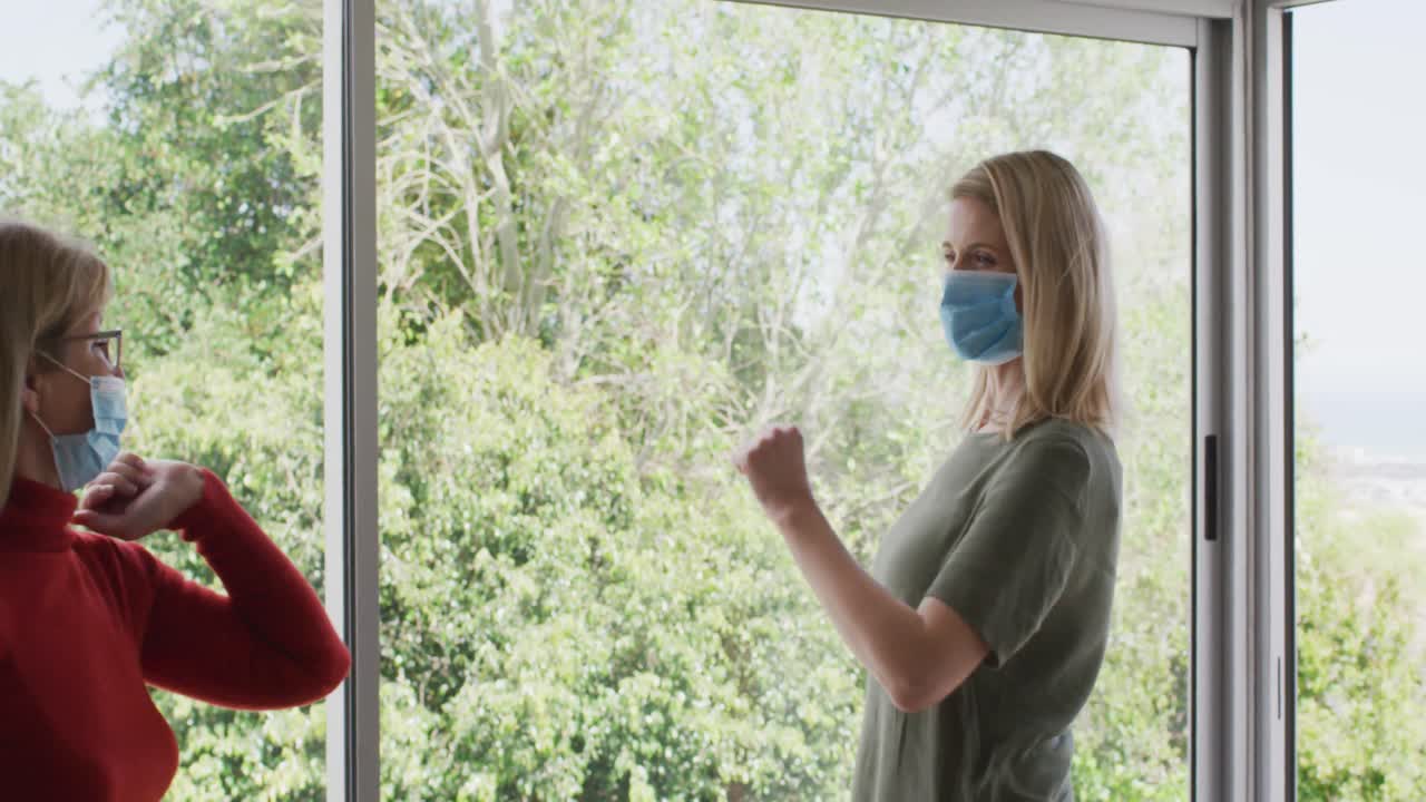 madre e hija con máscaras faciales tocando los codos a través del vidrio