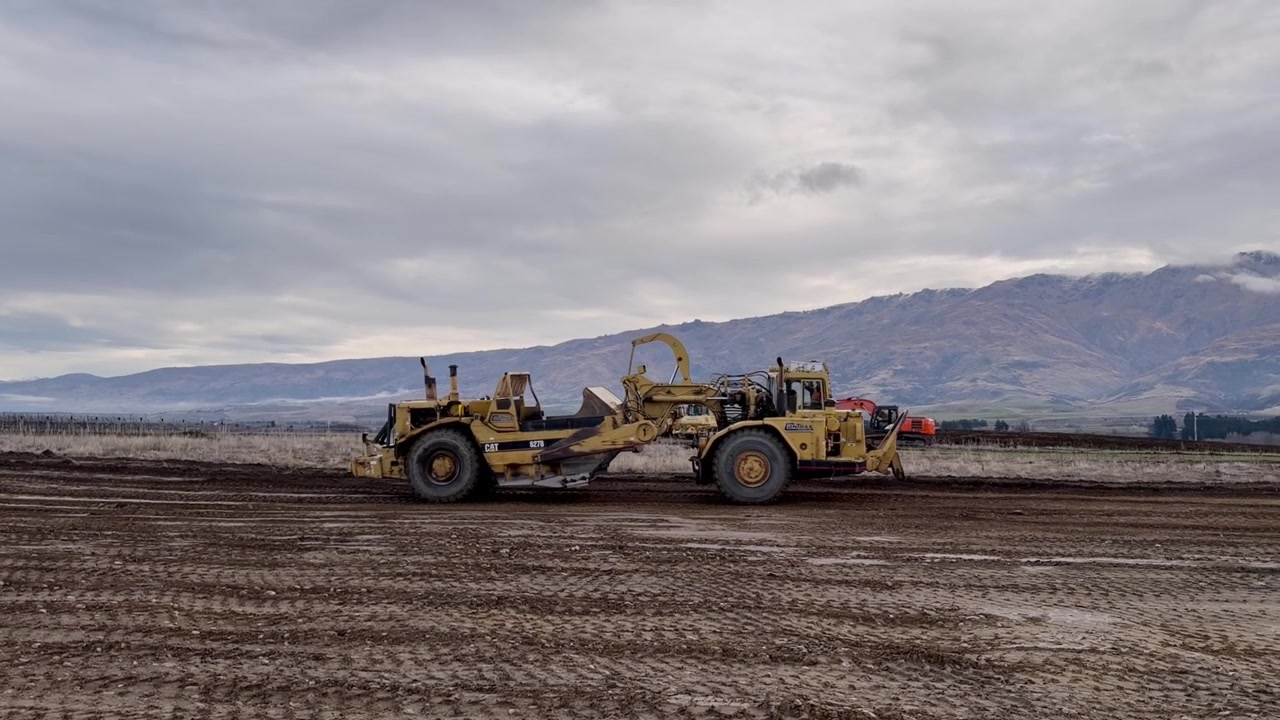 Heavy earthmoving machinery grades and levels open farmland for vineyard development in Central Otago, New Zealand. Scenic rural construction footage.