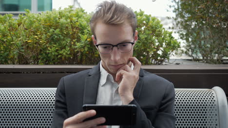 serious man sitting outside, watching movie on phone, thinking