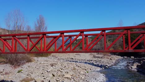 Drohnenschuss,-Der-Zur-Flussbrücke-Und-Den-Schneebedeckten-Bergen-Im-Hintergrund-Mit-Blauem-Himmel-Hinuntergeht