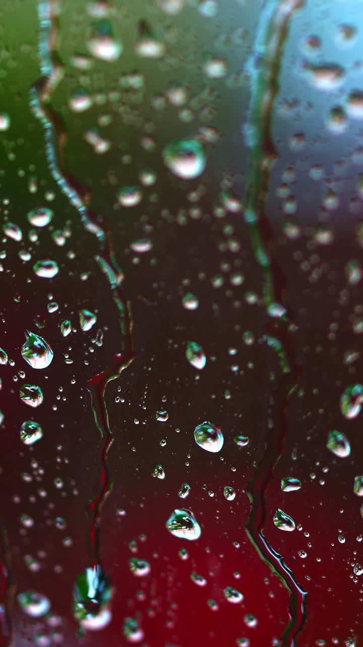 Rainy background on glass. Raindrops on window on blur background of bright dots. Drops of rain flow down the window. Drops of water drops on window pane. Vertical video
