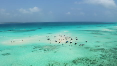 Anchored-boats-and-people-in-shallow-tropical-ocean-sandbank,-Zanzibar
