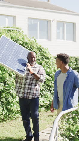 vertical video of african american father with solar panel and son talking in the sun, slow motion