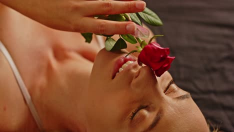 close up of an attractive woman lying in bed and sensually playing with a red rose