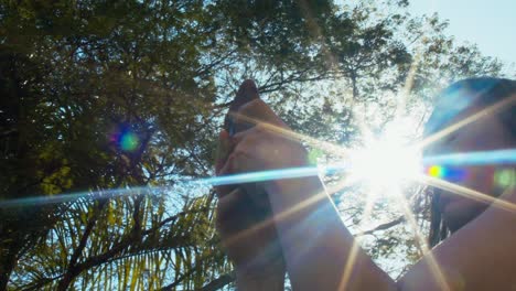 Handheld-shot-of-woman-with-a-cell-phone,-low-angle-against-sun-flare