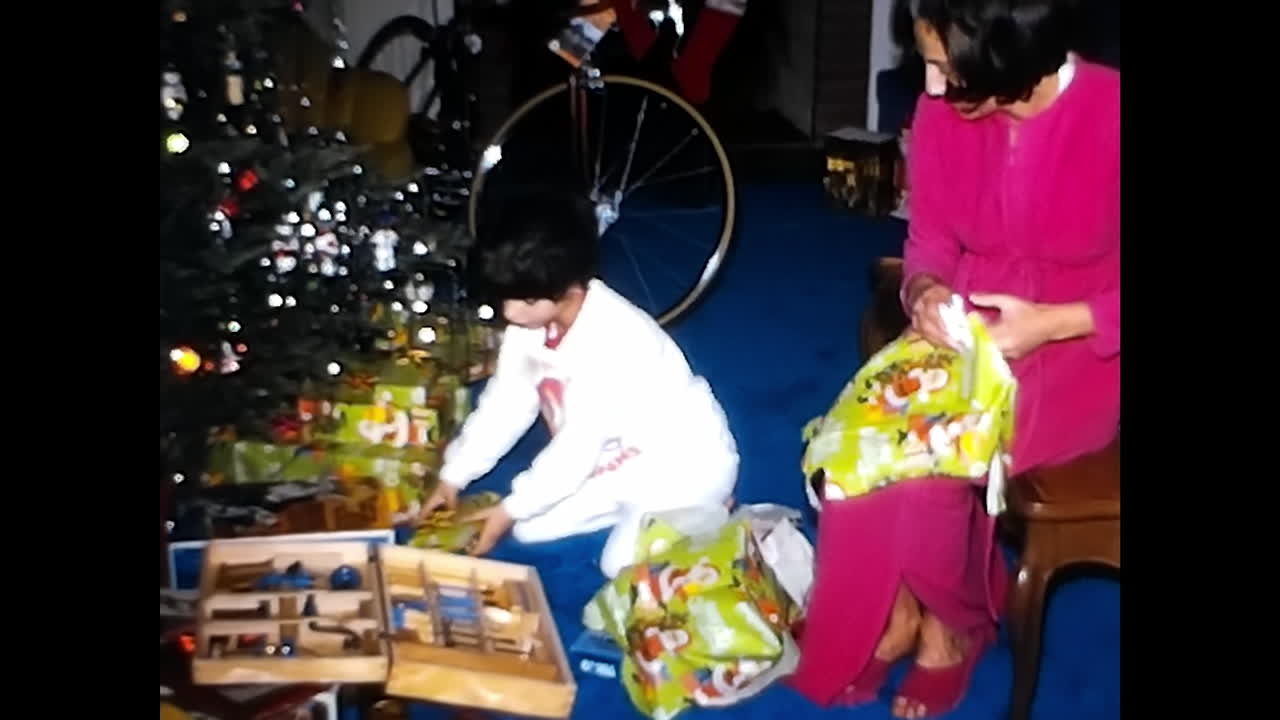 Young Boy Opening Christmas Present With Woman. CIRCA USA - 1970s: A young boy eagerly opens a Christmas present while standing next to a woman in this 1970s video archive from the USA.
