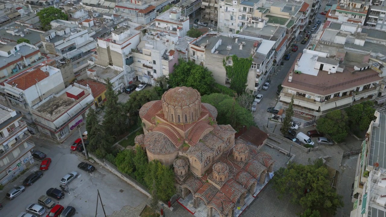 Primo piano aereo di una chiesa bizantina a croce con una cupola centrale e cupole più piccole raggruppate, immersa tra alberi e strade cittadine