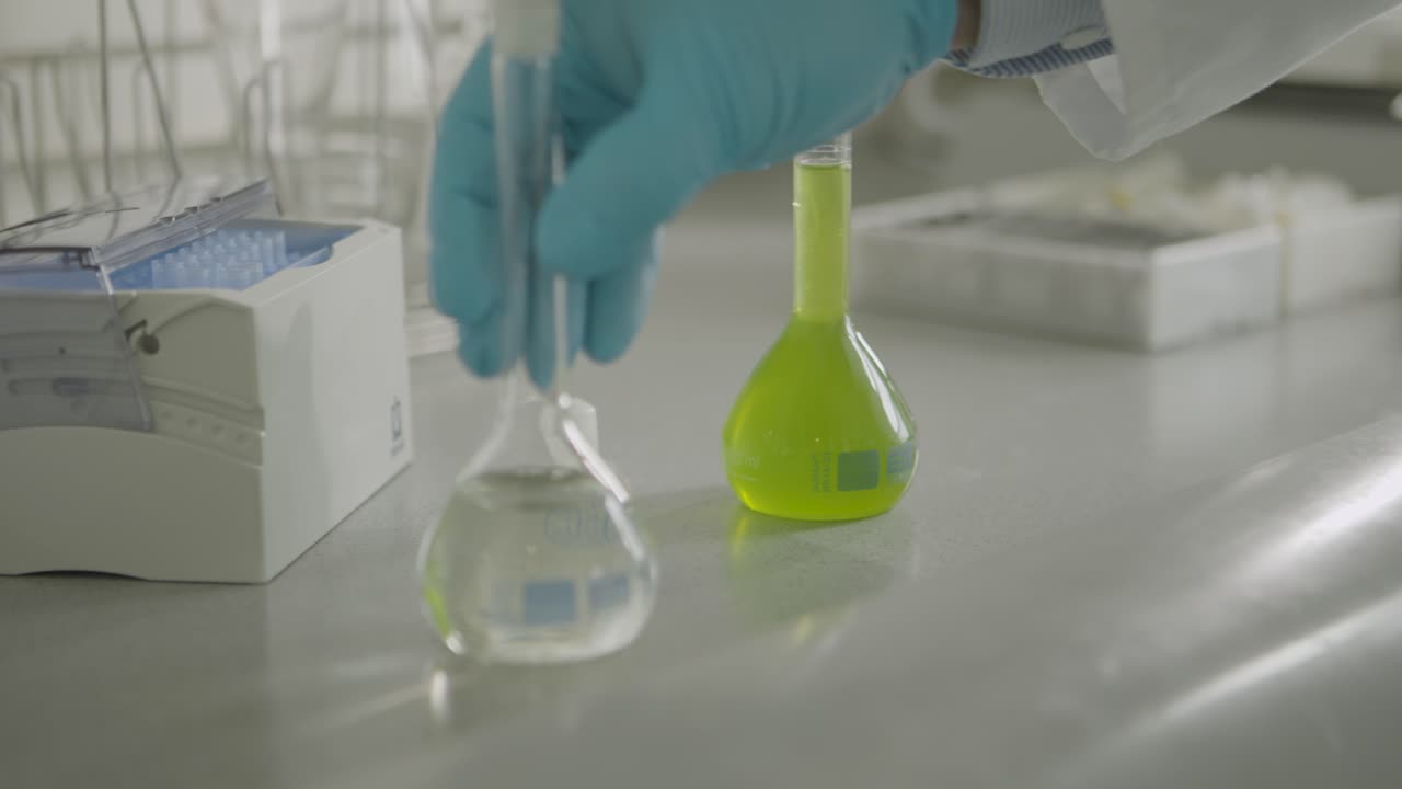 Scientist in lab coat examining liquid in flask with gloved hand for research purposes
