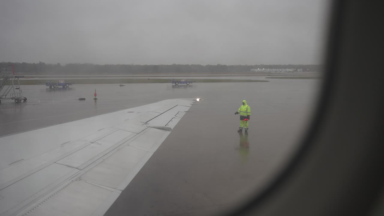 FPV rack focus from rainy airplane window to wing walker marshall on the airport tarmac - gloomy day