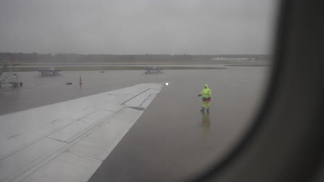 fpv rack focus from rainy airplane window to wing walker marshall on the airport tarmac - gloomy day