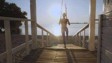 allenamento all'aperto. cinghie a sospensione. allenamento con cinghie. giovane donna atletica sta facendo esercizi di resistenza per tutto il corpo usando corde a loop trx, in spiaggia durante il tramonto o l'alba. allenamento fitness all'aperta. concetto di stile di vita sano. sport mattutino